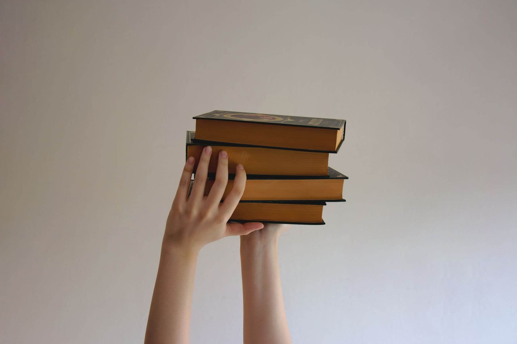 A hand holding up a small stack of hardback books.