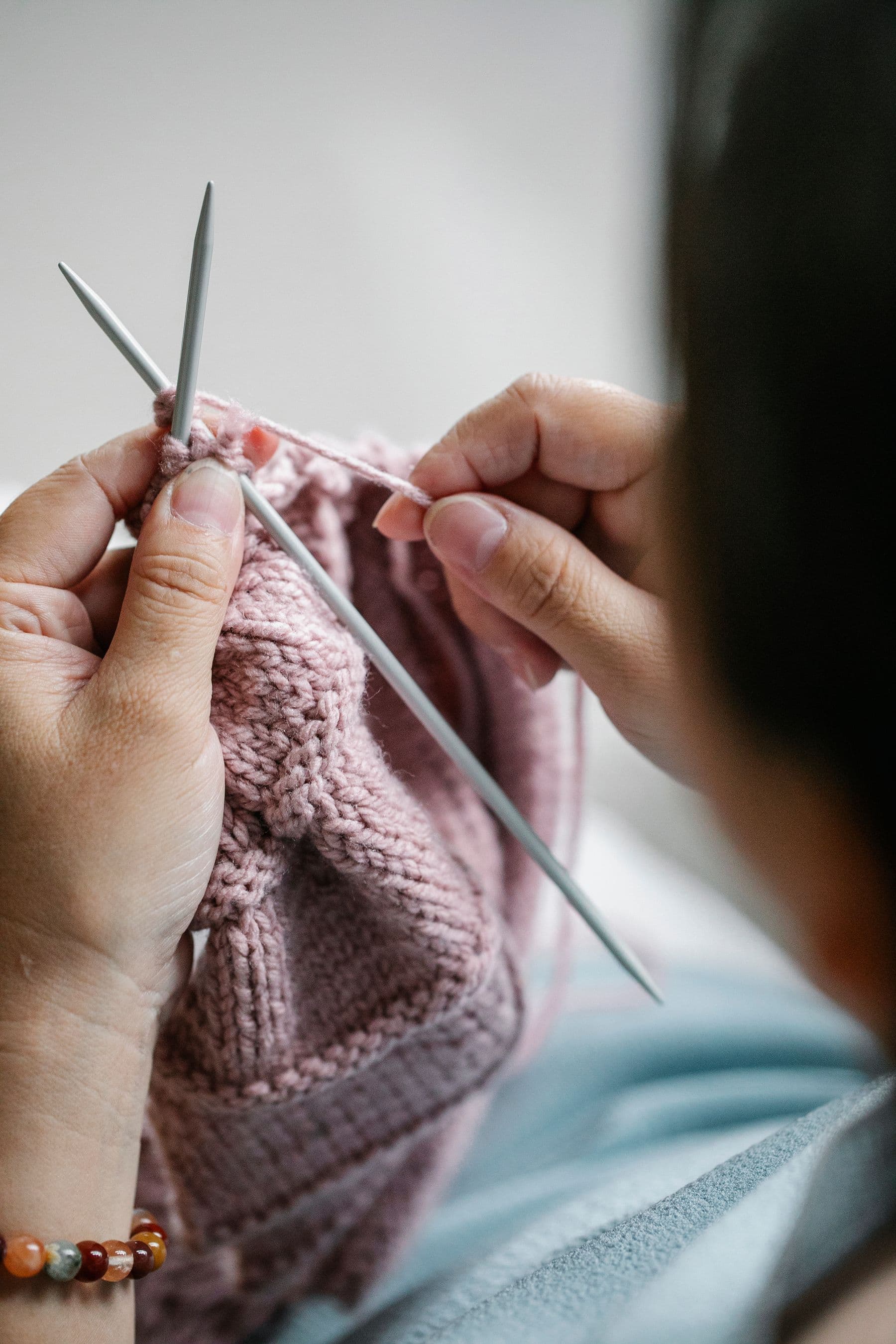Hands working a pair of knitting needles.