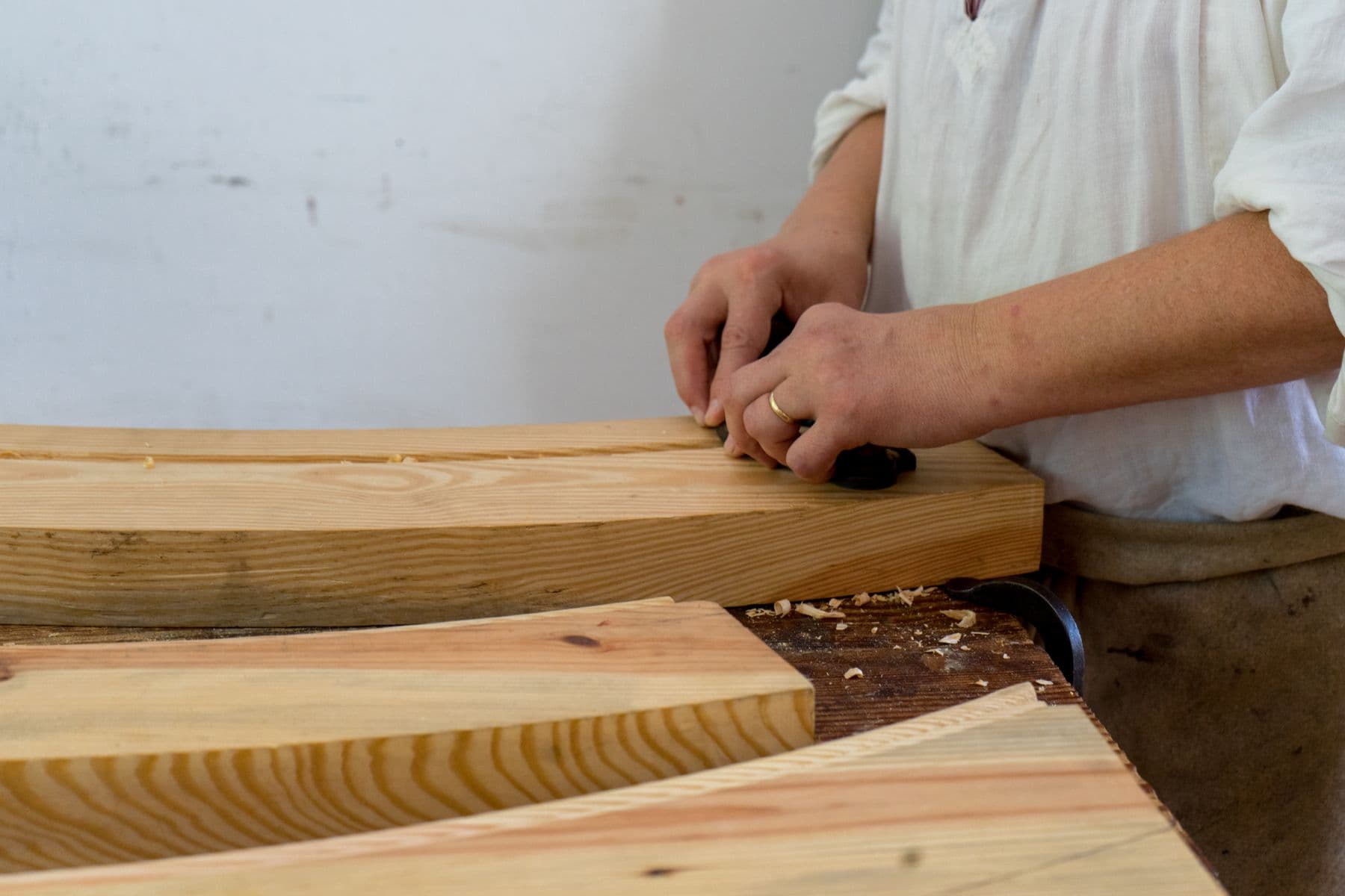Hands planing a length of timber at a workbench.