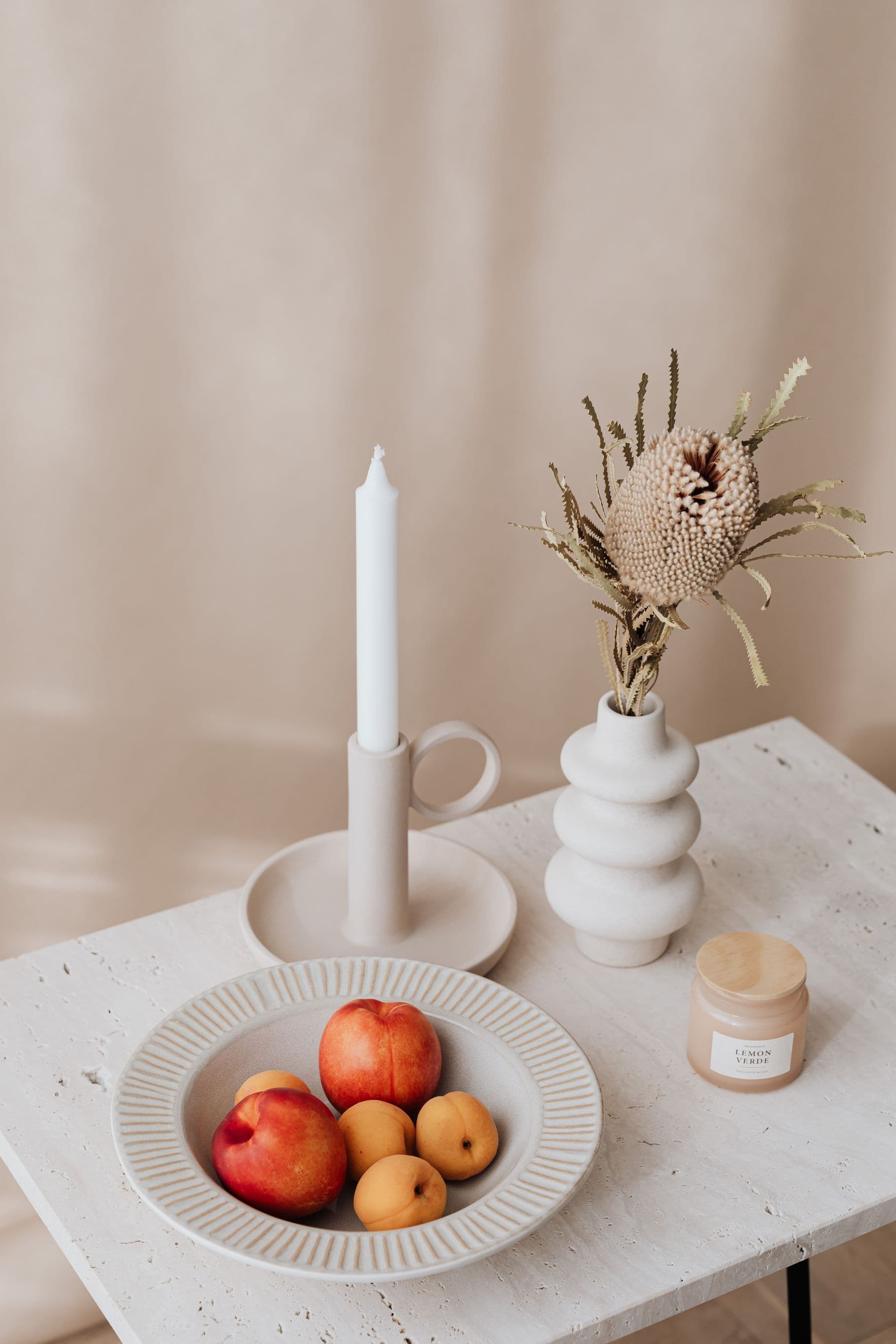 A candle and a vase of dried flowers on a table.