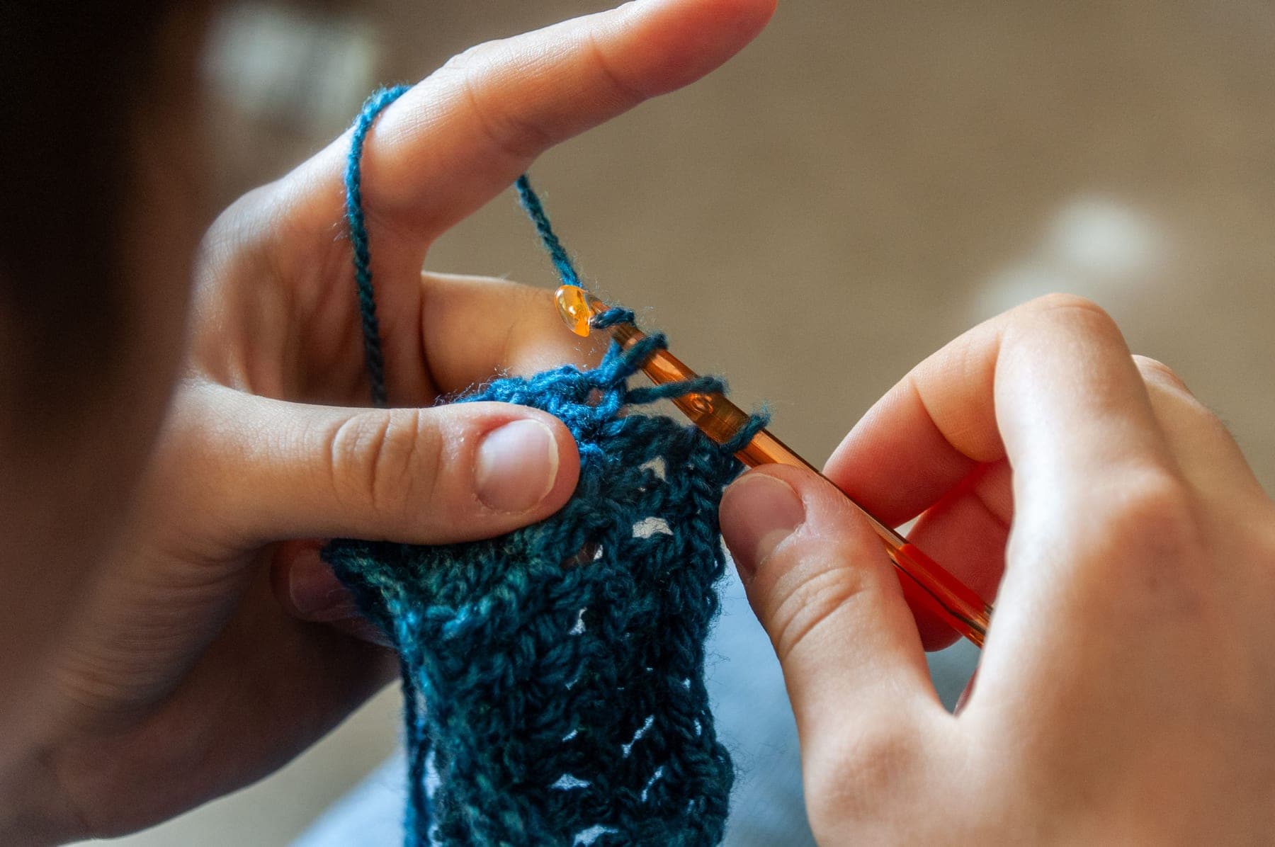 A child’s hands working a piece of teal wool with a hook.